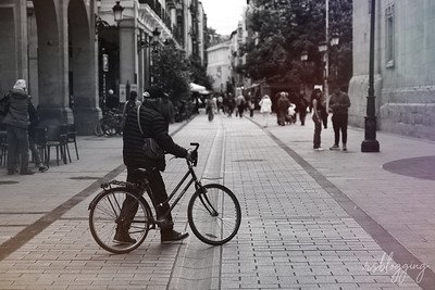 Persona empujando su bicicleta por una calle peatonal de Logroño, en blanco y negro, capturando un instante de vida urbana.