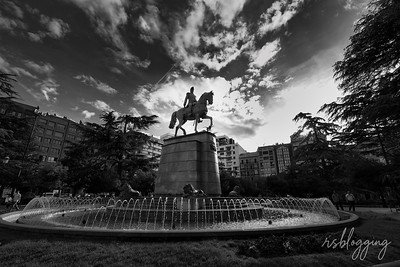 Estatua del General Espartero sobre su caballo al atardecer en blanco y negro, con fuente en primer plano y cielo dramático.